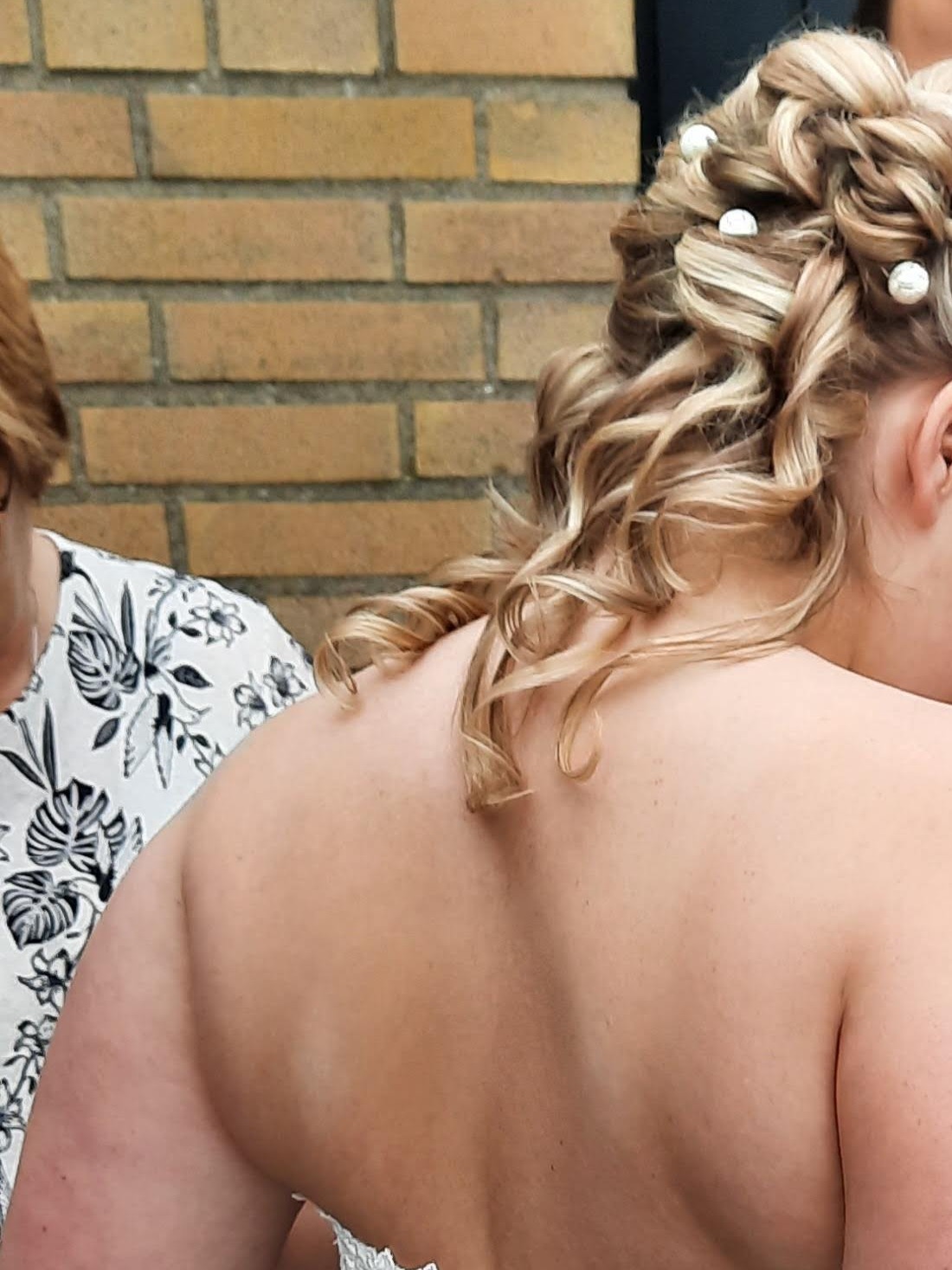 Blond opgestoken bruidskapsel met krullen en kleine witte versieringen, van achteren gezien